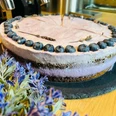 Heidelbeer-Lavendel-Torte auf schwarzer Platte, dekoriert mit Lavendel und Blaubeeren, neben Espressomaschine.