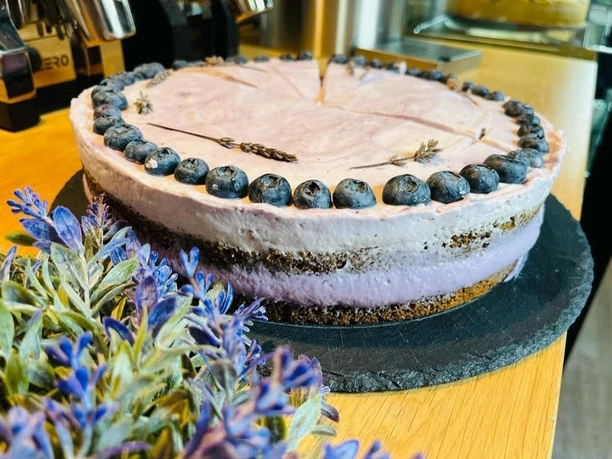 Heidelbeer-Lavendel-Torte auf schwarzer Platte, dekoriert mit Lavendel und Blaubeeren, neben Espressomaschine.