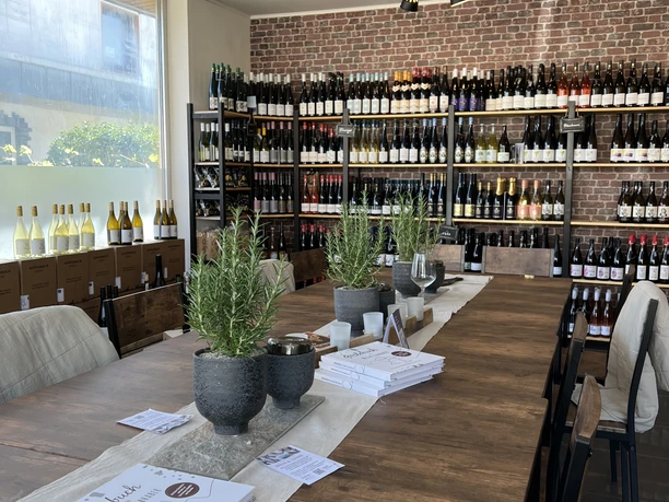 Bergischer Weinkeller Modernes Weinlokal mit hölzernem Tisch, Kräutertöpfen und Weinflaschenregalen an der Backsteinwand.