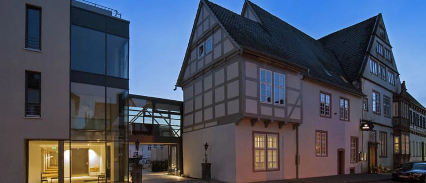 001_Hotel-Stadtpalais_Aussenansicht.jpg Abendliche Außenansicht eines modernen Gebäudetrakts neben einem historischen Fachwerkhaus.