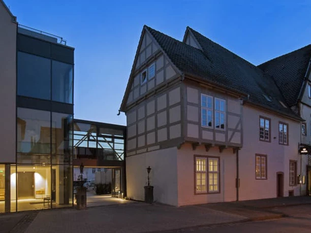 001_Hotel-Stadtpalais_Aussenansicht.jpg Abendliche Außenansicht eines modernen Gebäudetrakts neben einem historischen Fachwerkhaus.