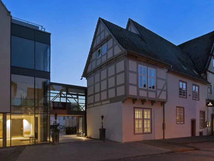 001_Hotel-Stadtpalais_Aussenansicht.jpg Abendliche Außenansicht eines modernen Gebäudetrakts neben einem historischen Fachwerkhaus.