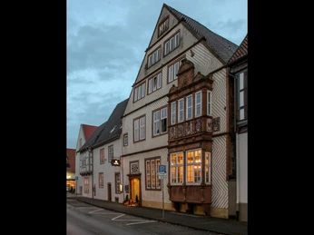 002_Hotel-Stadtpalais_Aussenansicht.jpg Historisches Gebäude im Fachwerkstil mit beleuchtetem Erker und markantem Satteldach.