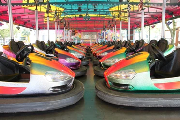 Bunte Autoscooter mit leuchtenden Farben stehen in zwei Reihen unter einem farbenfrohen Dach.