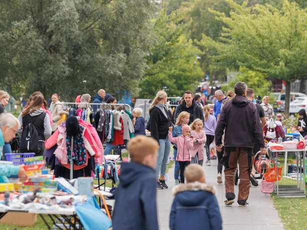 Kinderflohmarkt Bunte Stände entlang eines Parks mit Kindern und Familien, die Kleidung und Spielzeug erkunden.