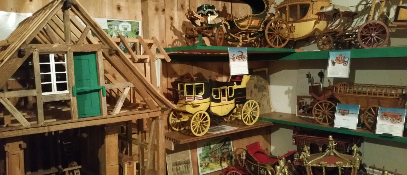 Mühlenmuseum Odenthal Miniaturmodelle historischer Kutschen und ein Fachwerkhaus aus Holz in einem rustikalen Raum.