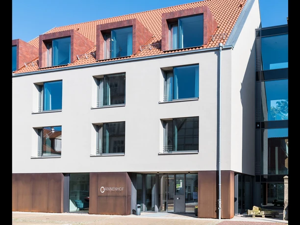 Moderner mehrstöckiger Hotelbau mit großen Fenstern, rotem Ziegeldach und eleganter Eingangstür.