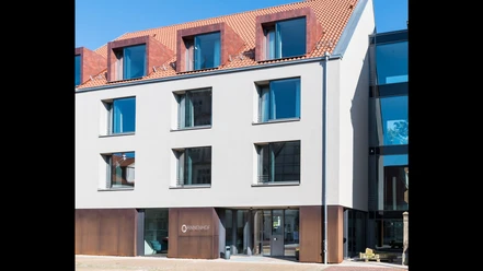001_Hotel-Annenhof_Aussenansicht.jpg Moderner mehrstöckiger Hotelbau mit großen Fenstern, rotem Ziegeldach und eleganter Eingangstür.