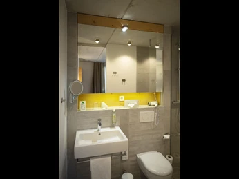 Modernes Badezimmer mit großen Spiegeln, weißem Waschbecken und Toilette; dezente Beleuchtung.