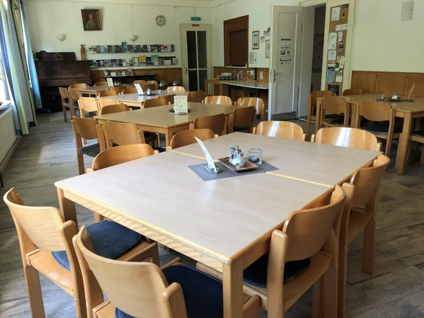 Bright dining room with wooden chairs and tables, decorated with information brochures and pictures on the walls.
