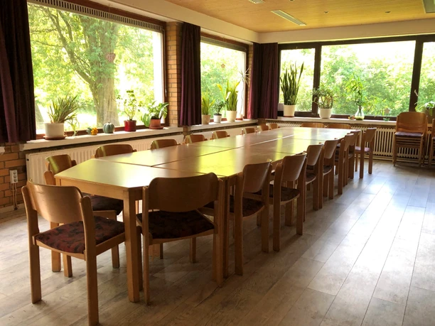 Bright room with large windows, wooden tables and lots of indoor plants offers space for events.