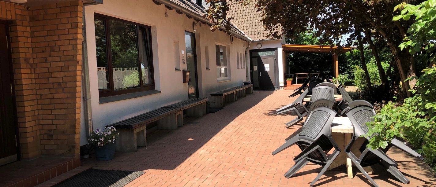 Außenansicht Op de foto zie je een geplaveide buitenruimte met bomen, banken en een aantal zwarte stoelen.