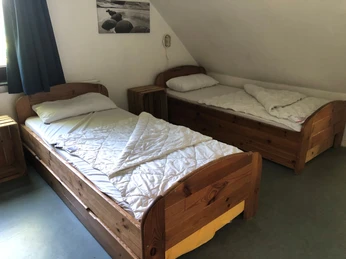 Zimmer Zwei holzgetäfelte Einzelbetten mit weißen Bettdecken in einem hellen Raum mit schräger Decke.