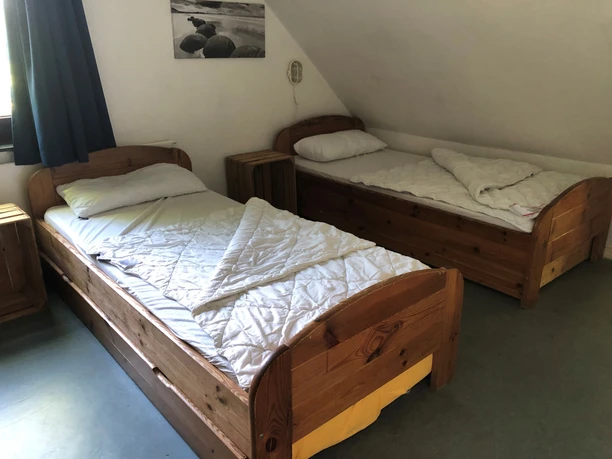 Zimmer Twee eenpersoonsbedden met houten panelen en witte dekbedden in een lichte kamer met een schuin plafond.