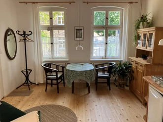 Am Johannistor.jpg Heller Essbereich mit Holzmöbeln, rundem Tisch und zwei Fenstern, die Tageslicht einlassen.