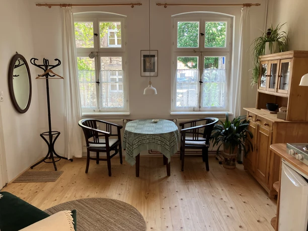 Am Johannistor.jpg Heller Essbereich mit Holzmöbeln, rundem Tisch und zwei Fenstern, die Tageslicht einlassen.