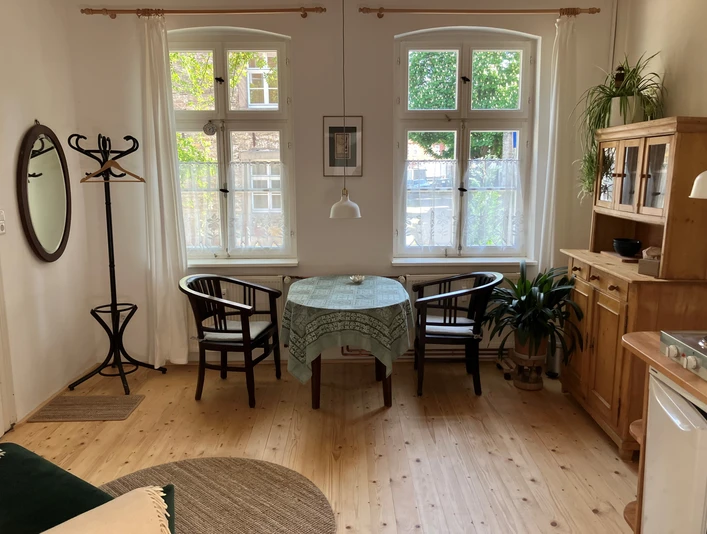 Am Johannistor.jpg Heller Essbereich mit Holzmöbeln, rundem Tisch und zwei Fenstern, die Tageslicht einlassen.