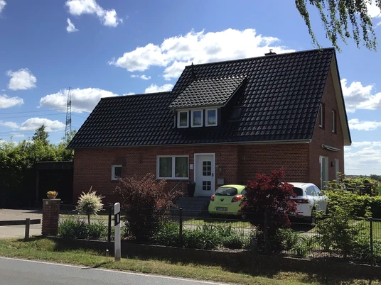 Backstein-Gästehaus Meyer vor blauem Himmel, mit Garten und zwei geparkten Autos im Vordergrund.Brick guest house Meyer in front of a blue sky, with garden and two parked cars in the foreground.Det murede gæstehus Meyer foran en blå himmel, med have og to parkerede biler i forgrunden.Bakstenen gastenverblijf Meyer voor een blauwe lucht, met tuin en twee geparkeerde auto's op de voorgrond.