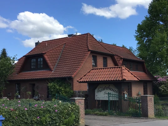 Gästehaus Lange Gästehaus Lange mit rotem Ziegeldach in grüner Umgebung und blauem Himmel im Hintergrund.