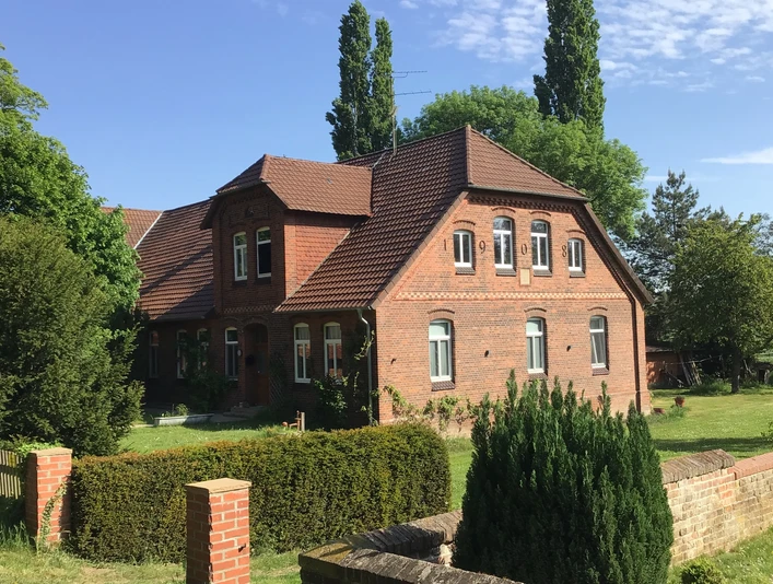 kloster-blick Ein rotes Backsteingebäude mit Satteldach steht vor einer Hecke, umgeben von grünen Bäumen und Rasen.A red brick building with a pitched roof stands in front of a hedge, surrounded by green trees and lawn.En rød murstensbygning med skråt tag står foran en hæk, omgivet af grønne træer og græsplæne.Een rood bakstenen gebouw met een schuin dak staat voor een heg, omringd door groene bomen en gazon.