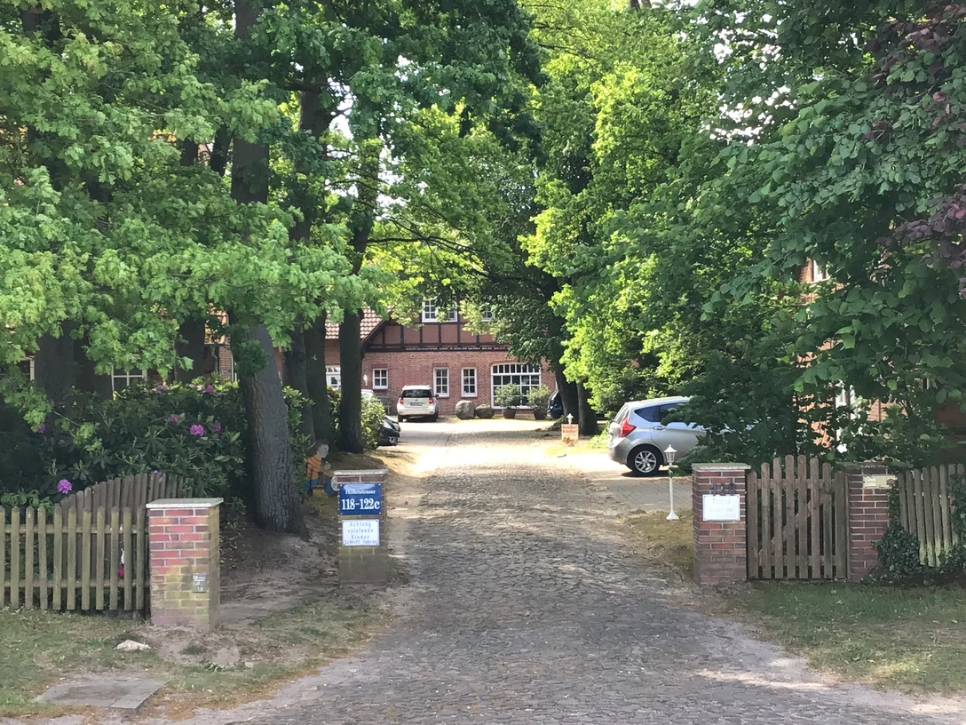 Ein einladender Hof mit Backsteingebäuden und umgebenden Bäumen, ein Auto parkt auf Kopfsteinpflaster.