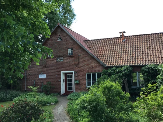 FeWo Strump Rotes Backsteinhaus mit rotem Ziegeldach und begrüntem Garten, umgeben von üppiger Vegetation.