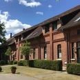 Gästehaus Schlossgarten Backsteingebäude mit markanten Giebeln und gepflegtem Vorgarten bei blauem Himmel und Sonnenschein.