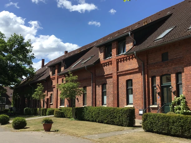 Gästehaus Schlossgarten Backsteingebäude mit markanten Giebeln und gepflegtem Vorgarten bei blauem Himmel und Sonnenschein.