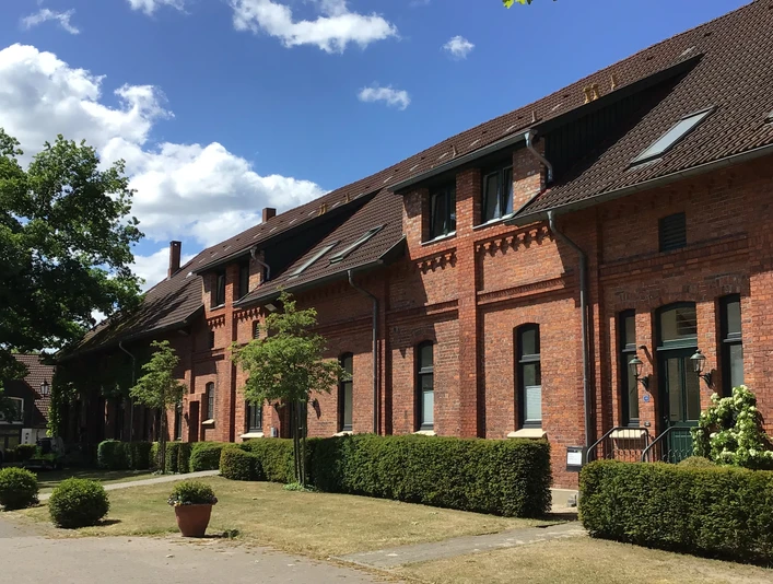 Gästehaus Schlossgarten Backsteingebäude mit markanten Giebeln und gepflegtem Vorgarten bei blauem Himmel und Sonnenschein.
