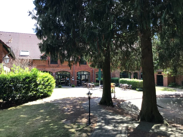 Red brick building with seating in the inner courtyard, surrounded by tall trees and hedges.
