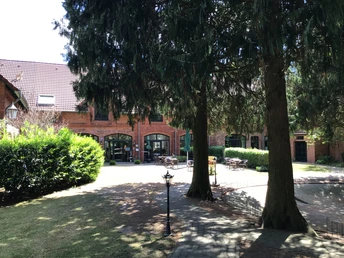 Gästehaus Schlossgarten Rotes Backsteingebäude mit Sitzgelegenheiten im Innenhof, umgeben von hohen Bäumen und Hecken.