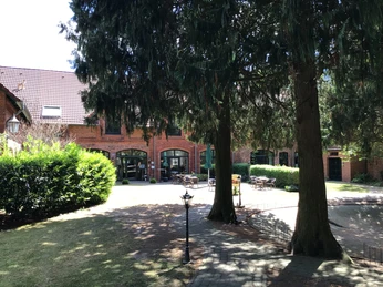 Gästehaus Schlossgarten Rotes Backsteingebäude mit Sitzgelegenheiten im Innenhof, umgeben von hohen Bäumen und Hecken.
