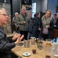 Menschen genießen ein Kaffeetasting. Ein Barista erklärt die Zubereitung, während Teilnehmer interessiert lauschen.
