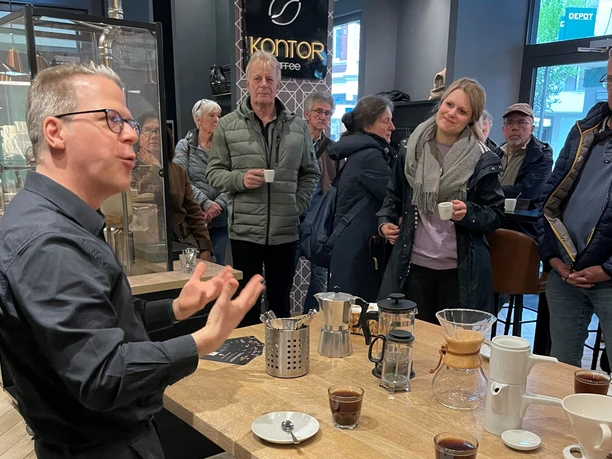 Menschen genießen ein Kaffeetasting. Ein Barista erklärt die Zubereitung, während Teilnehmer interessiert lauschen.