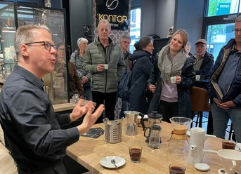 Kaffeetasting im Kaffeekontor Herford_Pro Herford GmbH.jpg Menschen genießen ein Kaffeetasting. Ein Barista erklärt die Zubereitung, während Teilnehmer interessiert lauschen.