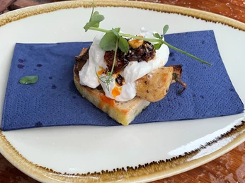 Ein kunstvoll angerichteter Snack mit pochiertem Ei, Trüffel, Pilzen und Kräutern auf Toastbrot.