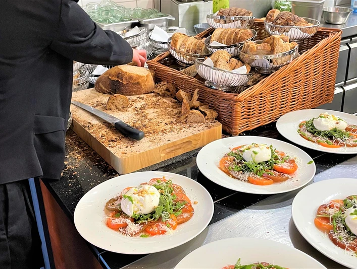 Kulinarische Führung_Elsbach-Restaurant-Pro Herford GmbH.jpg Ein Kellner richtet in einer Restaurantküche auf Tellern präzise angerichtete Speisen an.