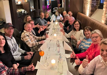 Gesellige Runde-Kulinarische Führung-Pro Herford GmbH.jpg Menschen sitzen an langer Tafel in einem Restaurant und lächeln, während sie die Atmosphäre genießen.
