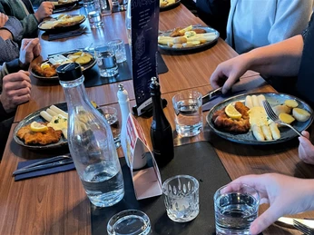 Mehrere Personen sitzen an einem Tisch und genießen Teller mit Schnitzel, Spargel und Kartoffeln.