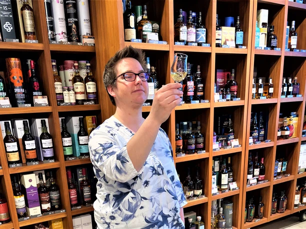 Tasting bei Maxi Schuser-Pro Herford GmbH.JPG Person verkostet Spirituose in einem gut sortierten Laden mit vielen verschiedenen Flaschen im Regal.