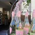 Bergischer Weinkeller Rosa etikettierte Weinflaschen stehen in einer offenen Holztür unter einer blühenden Dekoration.