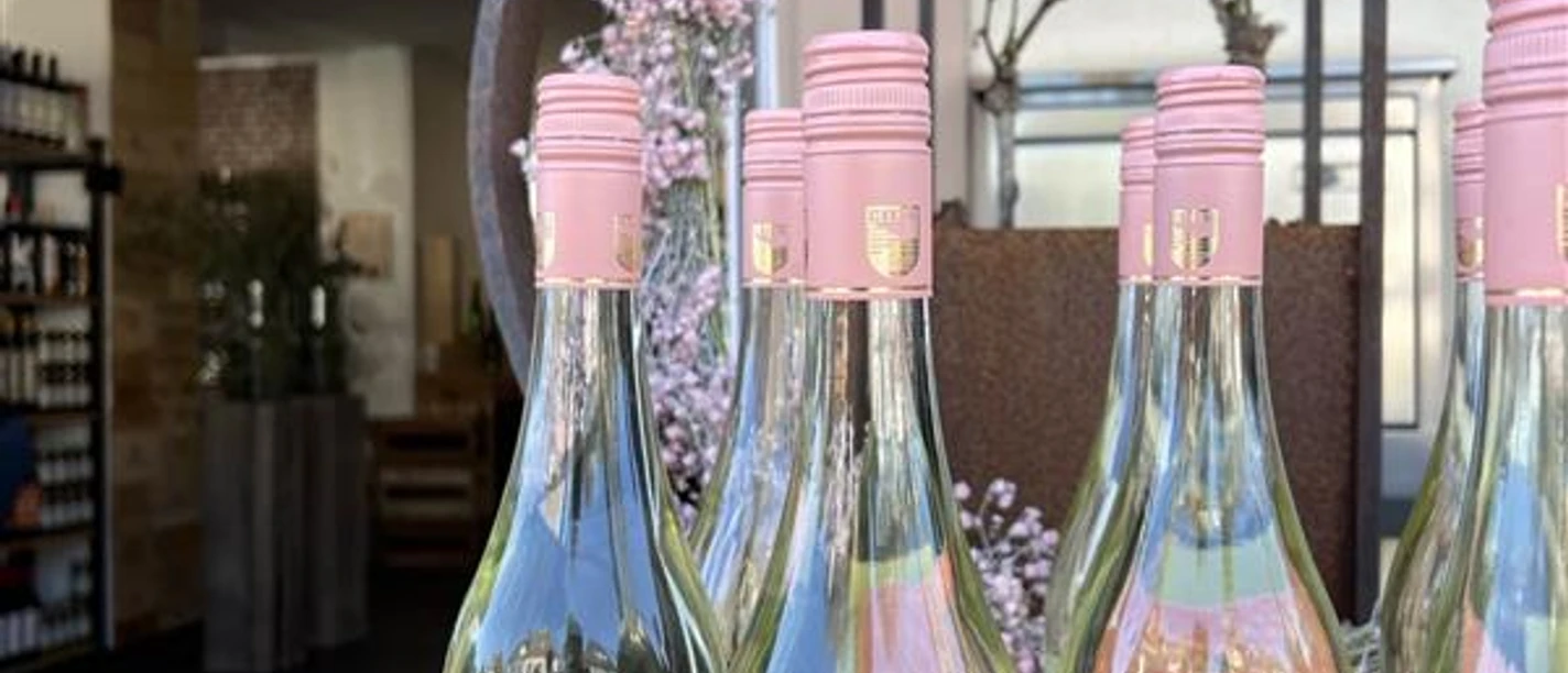 Bergischer Weinkeller Rosa etikettierte Weinflaschen stehen in einer offenen Holztür unter einer blühenden Dekoration.