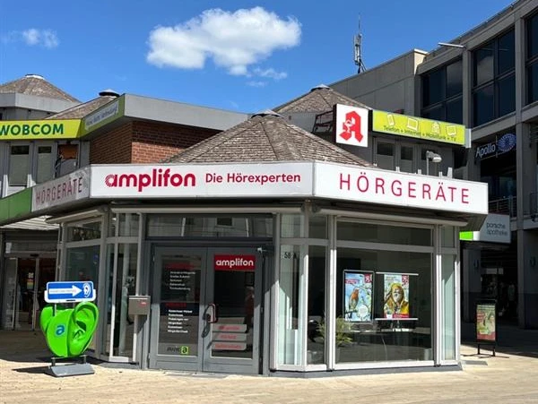Amplifon.jpg Das Bild zeigt ein modernes Geschäft von Amplifon, spezialisiert auf Hörgeräte, mit auffälliger, roter Beschilderung und großflächigen Fenstern.