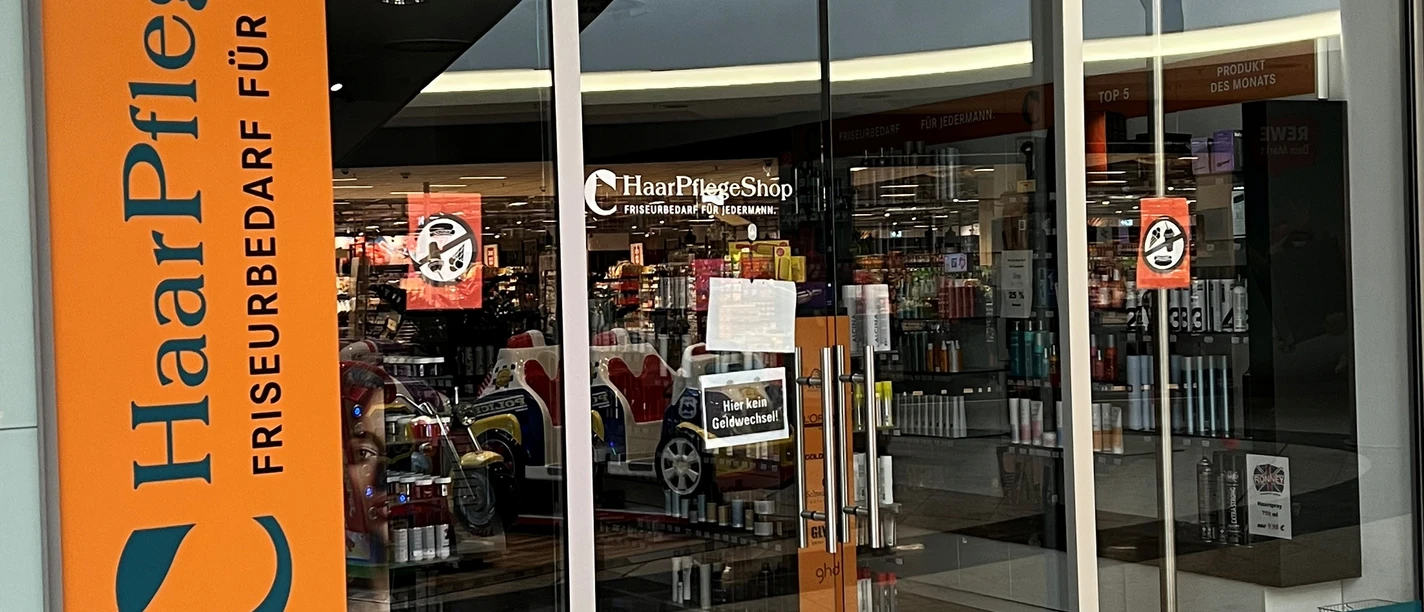 Haarpflegeshop.jpg Eingang eines Haarpflege-Shops mit Friseurbedarf und Markenlogos wie Wella, L'Oréal und Schwarzkopf.