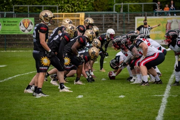 Paderborn Dolphins Football.jpg Zwei American-Football-Teams stehen sich bereit für den Spielbeginn auf einem grünen Spielfeld gegenüber.