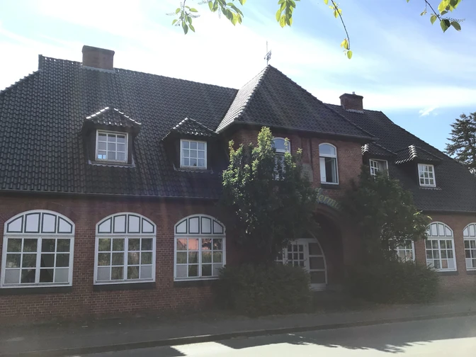 Historisches Backsteingebäude mit großen Sprossenfenstern und einem begrünten Eingangsbereich.