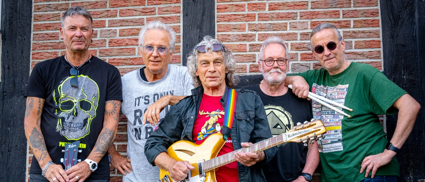 Lars-and-Friends (3).jpg Fünf Musiker stehen vor einer Backsteinmauer, mit Gitarren und lässiger Freizeitkleidung.