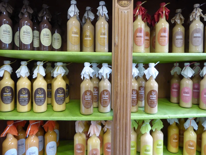 Heitmanns Eierlikörparadies Regale voller bunter Likörflaschen mit dekorativen Schleifen, aufgereiht in einem Laden.