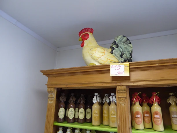 Großer Keramikhahn auf einem Holzregal mit Flaschen von Apfelsaft oder Getränken in einem Geschäft.