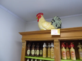 Heitmann_3.JPG Großer Keramikhahn auf einem Holzregal mit Flaschen von Apfelsaft oder Getränken in einem Geschäft.